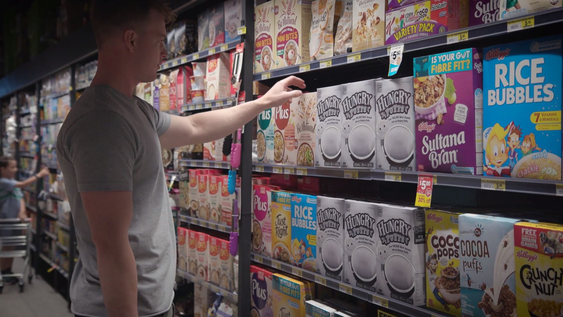 A man picking a box of Hungry Puffs cereal from a supermarket shelf
